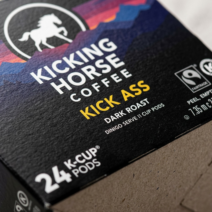 Extreme macro view captures the rich matte black ink texture and sharp, precise white and gold printing on the Kicking Horse Kick Ass coffee pod box.